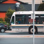 Ônibus urbano circula por uma rua movimentada, entre carros e edifícios.