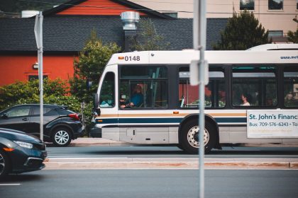 Ônibus urbano circula por uma rua movimentada, entre carros e edifícios.