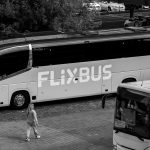 Ônibus rodoviário estacionado em um terminal, com passageiros nas proximidades.