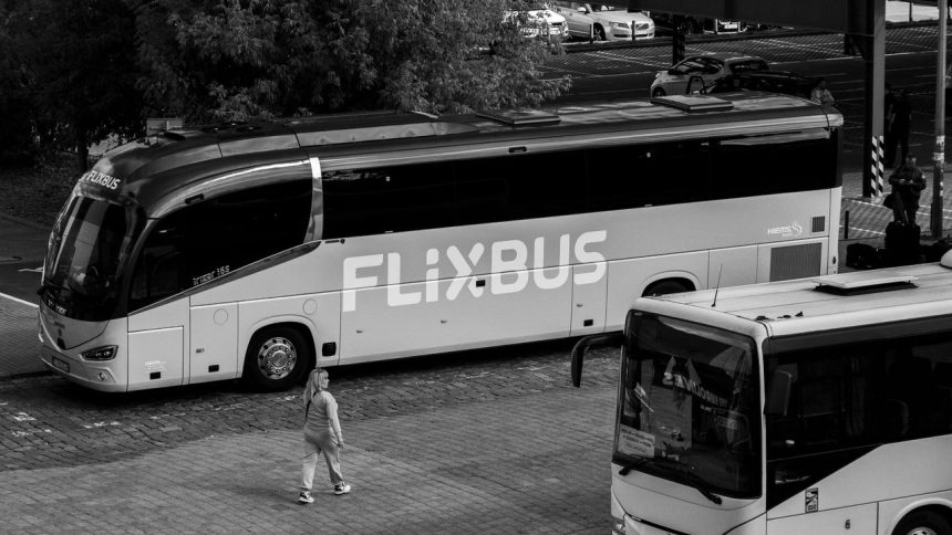 Ônibus rodoviário estacionado em um terminal, com passageiros nas proximidades.