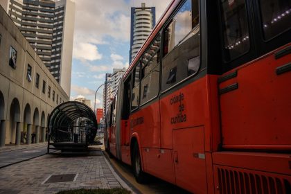 Ônibus urbano vermelho parado em um ponto moderno no centro de Curitiba.