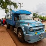 Ônibus azul de transporte público parado em uma rua, com passageiros embarcando e desembarcando.