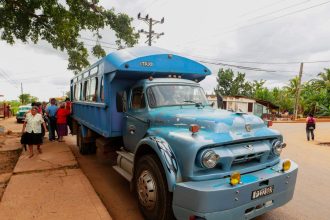 Ônibus azul de transporte público parado em uma rua, com passageiros embarcando e desembarcando.