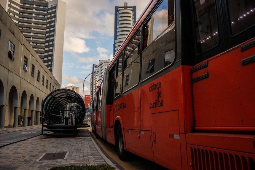 Ônibus urbano vermelho parado em um ponto moderno no centro de Curitiba.